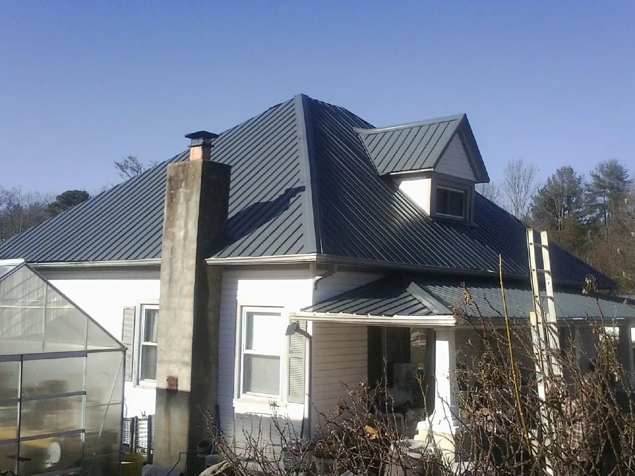 Dark blue standing seam metal roof on a white farmhouse with dormer — Slate & Tile Roof Repair by Roofing Brothers in Cut Off