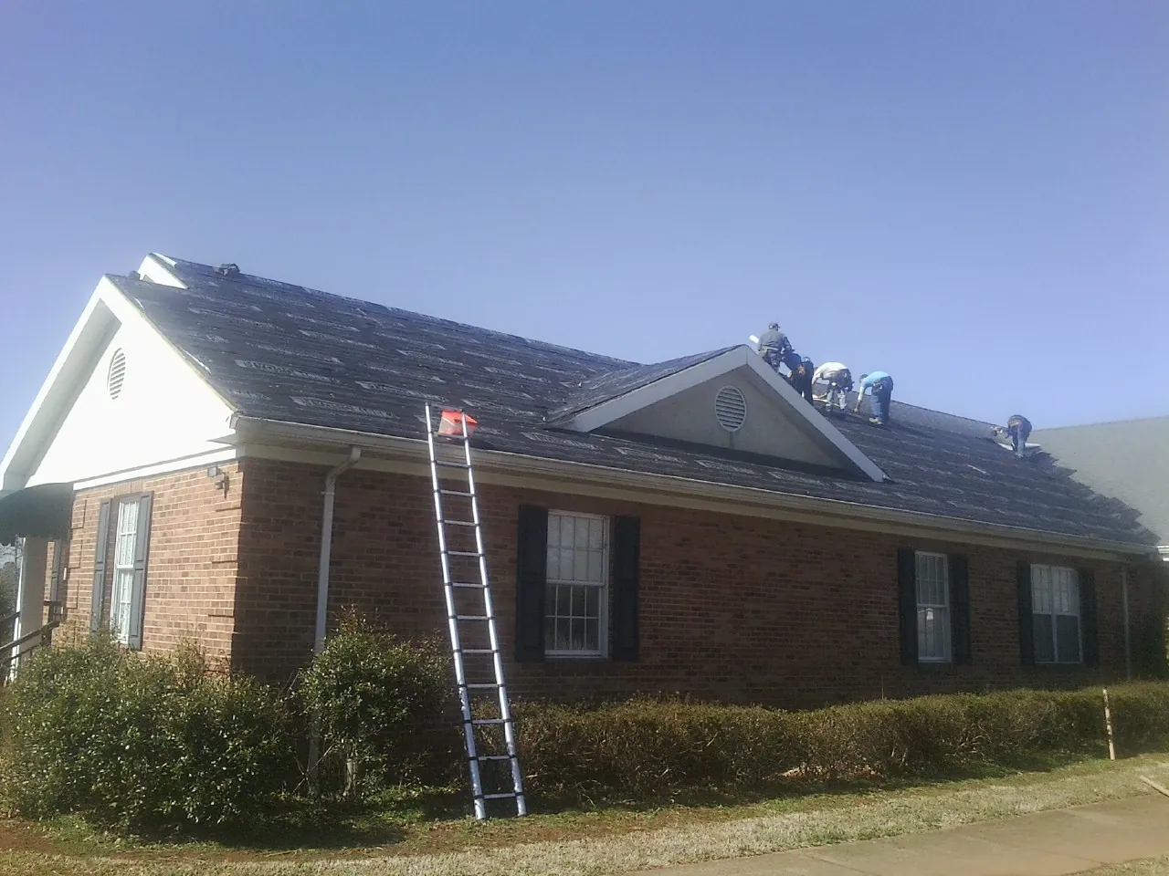 Crew tearing shingles off a brick ranch roof with a ladder set — Emergency Roof Repair work by our crew in Cut Off