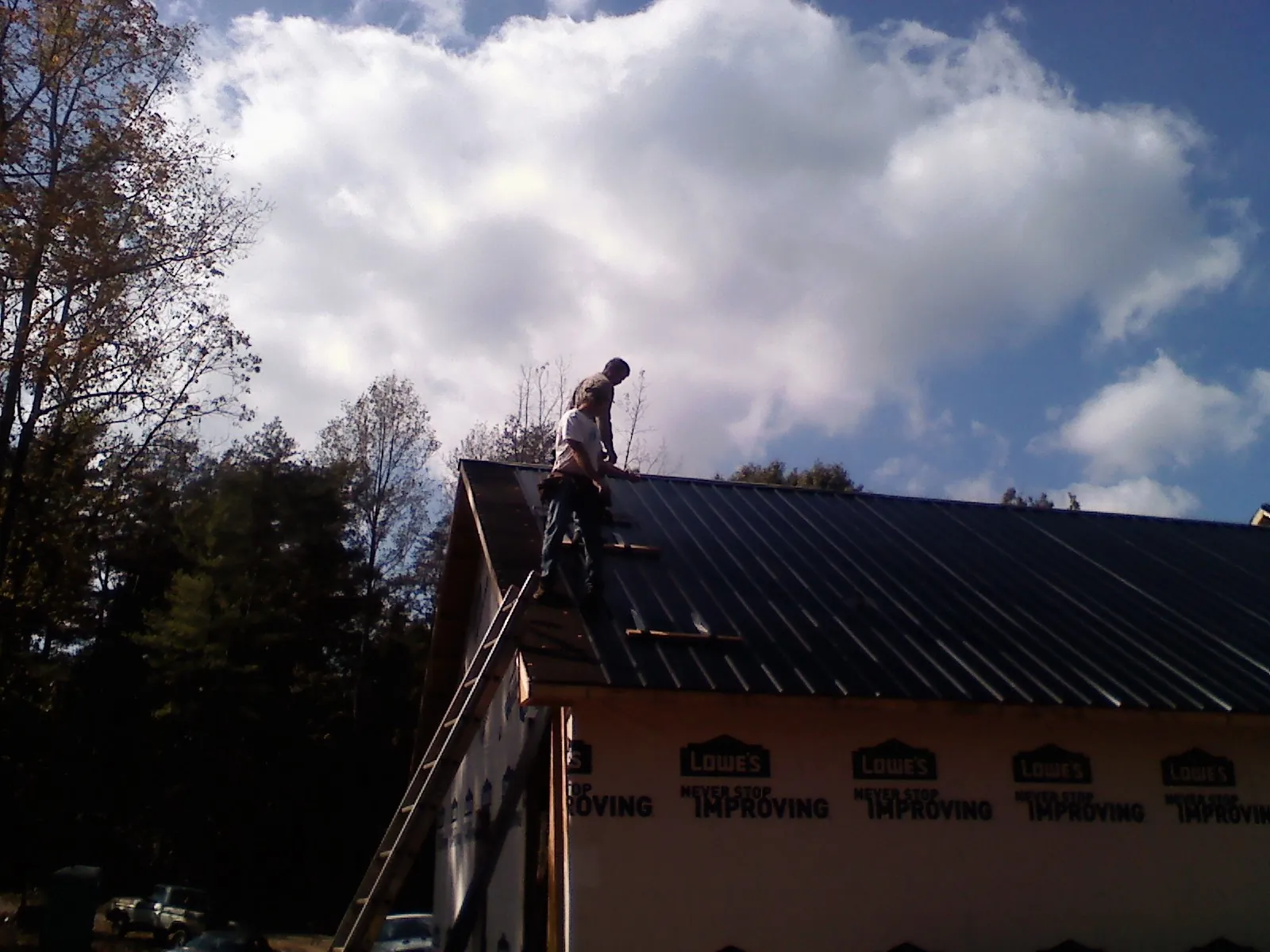 Roofer fastening dark metal panels high against a cloudy sky, from a Roof Inspection job in Cut Off
