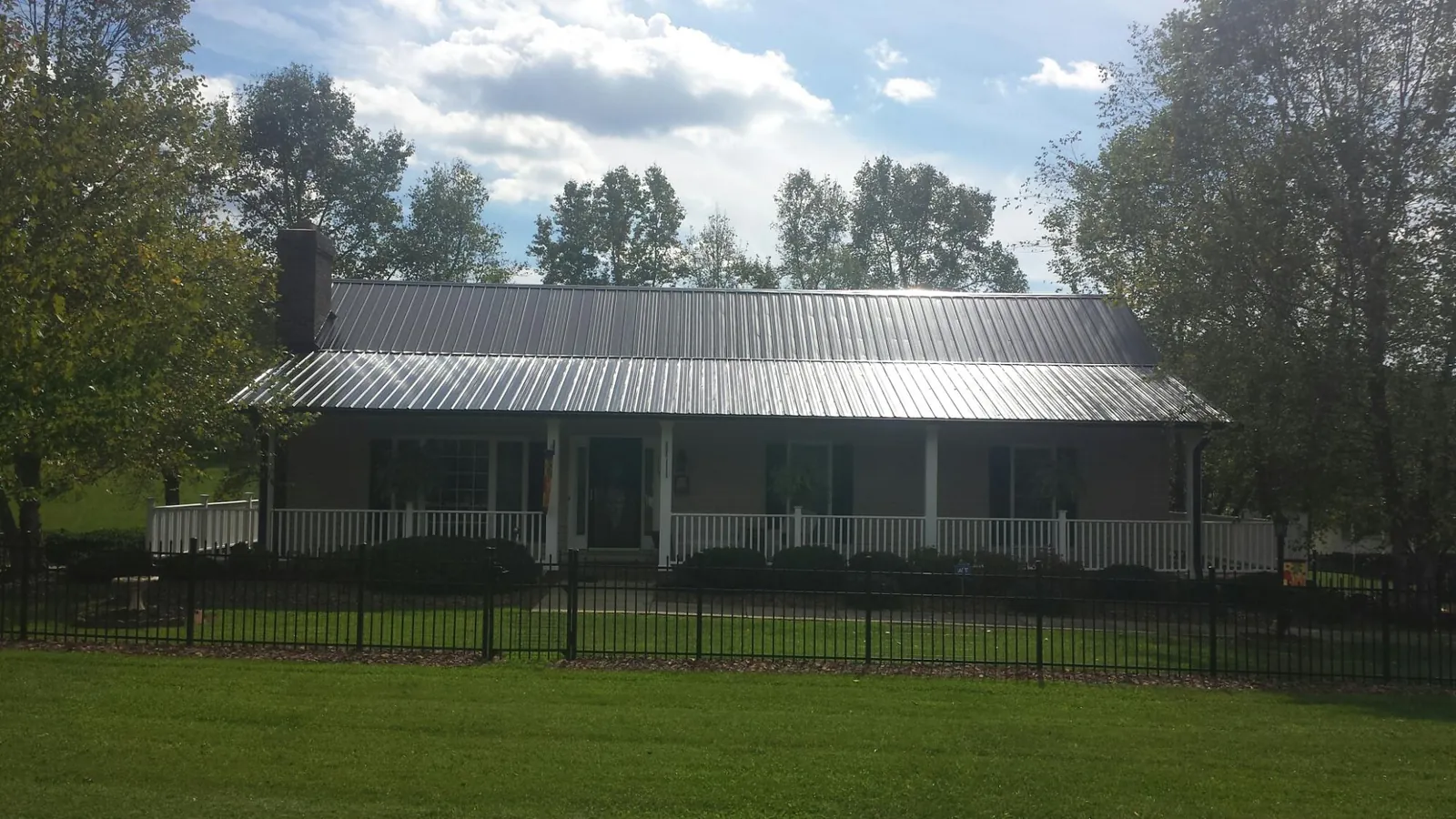 Gray metal roof on a brick ranch with a full width front porch — Gutter Guard Installation work by our crew in Cut Off