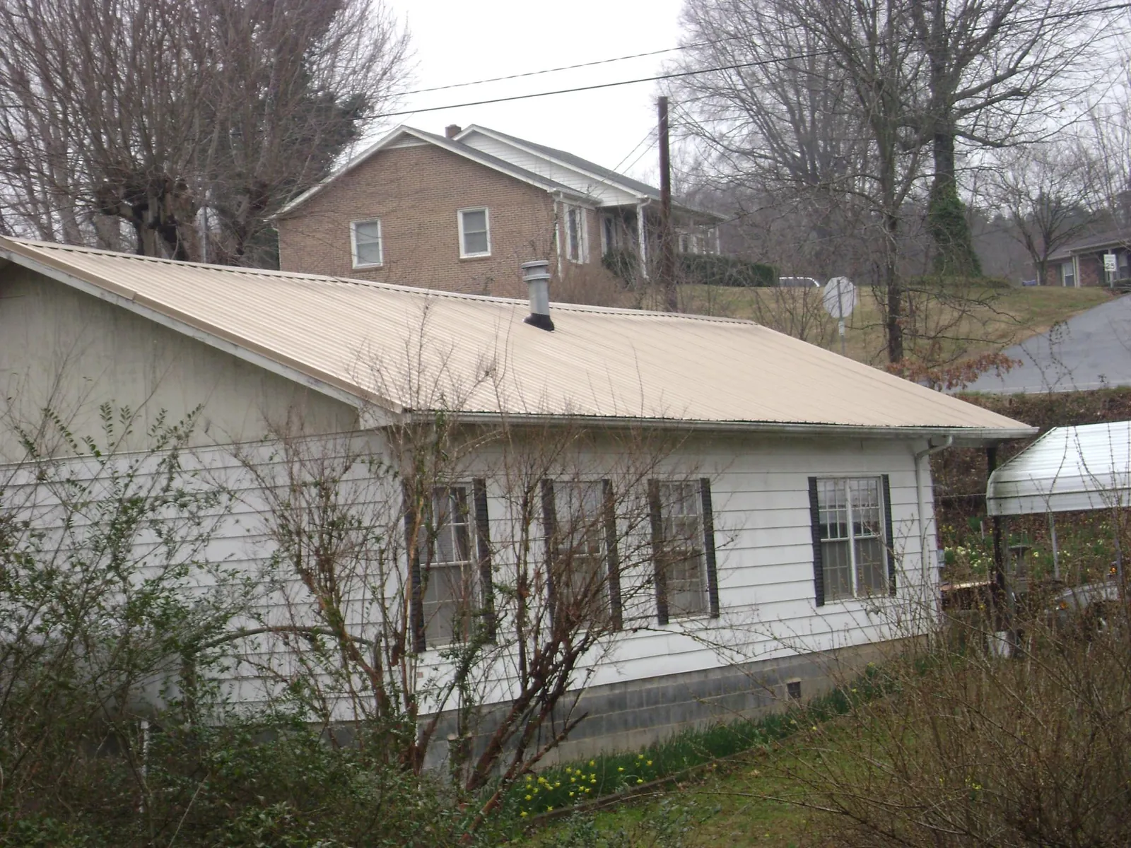 Tan metal roof on a white sided house set into a hillside — Commercial Roofing by Roofing Brothers in Cut Off