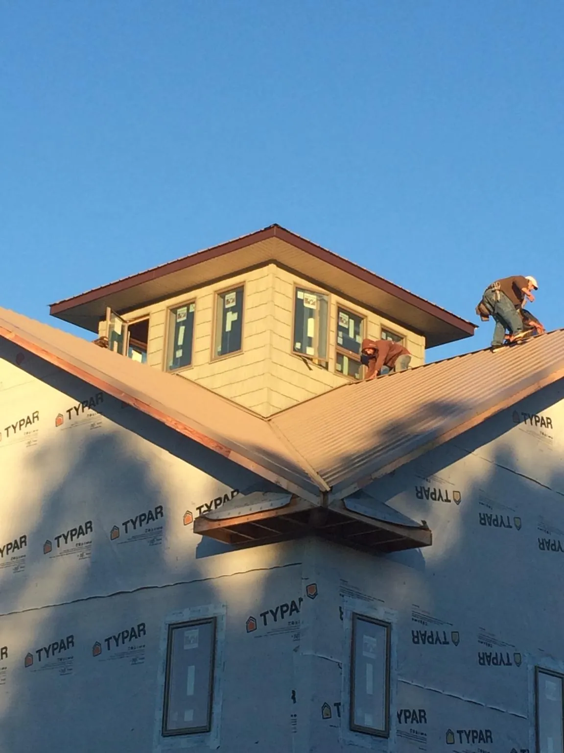 Roofers working around a rooftop cupola on a new metal roof at sunset — Roof Waterproofing in Cut Off by Roofing Brothers